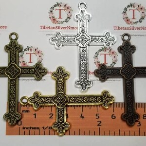 May include: Three ornate metal cross charms in silver, gold, and bronze. The crosses are approximately 2 inches in length and feature intricate designs.
