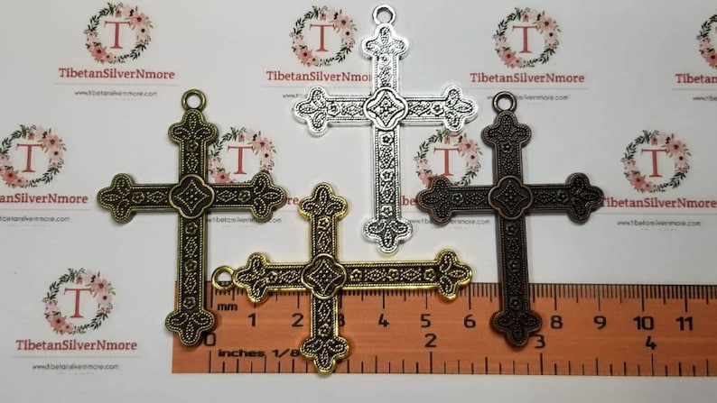 May include: Three ornate metal cross charms in silver, gold, and bronze. The crosses are approximately 2 inches in length and feature intricate designs.