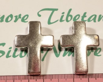 May include: Two silver metal cross charms. The crosses are flat and have a slightly textured surface.