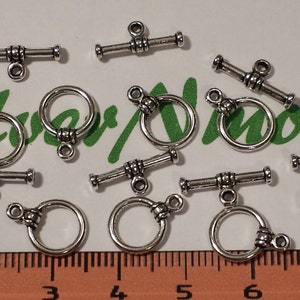 May include: Silver toggle clasps with a round ring. The clasps are silver in color and have a decorative design. There are 12 clasps in total.