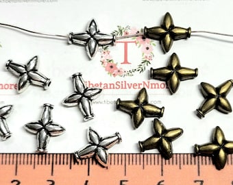 May include: A close-up of 10 silver and gold metal star-shaped beads. The beads are approximately 1 cm in diameter and have a hole in the centre for stringing. The beads are arranged on a white surface with a ruler in the background.