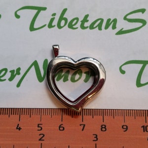 May include: Silver heart-shaped locket pendant with a hinged opening. The locket is approximately 2 inches in diameter.
