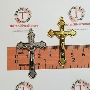 May include: Two silver and gold crucifixes with a black Jesus figure. The crucifixes are 2 inches tall and are measured against a ruler.