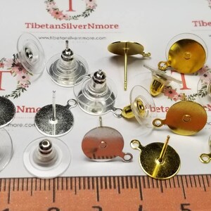 May include: Assortment of earring findings in gold and silver tones. The findings include post backs, lever backs, and jump rings. The findings are shown on a ruler with measurements in millimeters.