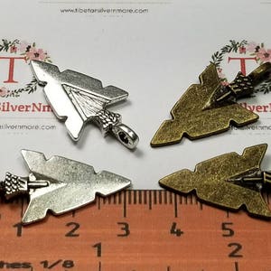May include: Four arrowhead charms, two silver and two bronze, with a ruler for size reference. The charms are approximately 2 inches long.