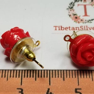 May include: A pair of red rose earrings with gold-tone findings. The earrings are about 1 inch in diameter.