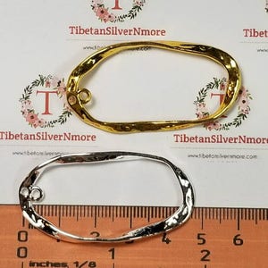 May include: Two metal oval-shaped frames, one gold and one silver, with a hammered texture. The frames are approximately 2 inches long and 1 inch wide. A ruler is included for size reference.