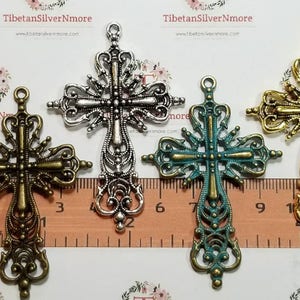 May include: Four ornate metal cross charms in different finishes: silver, bronze, turquoise, and gold. The crosses are approximately 2 inches tall and feature intricate details.