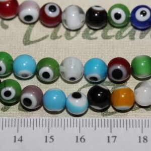 Puede incluir: Una hebra de cuentas de vidrio de colores con un diseño de ojo turco. Las cuentas tienen aproximadamente 1 cm de diámetro y están enhebradas en un hilo transparente. Las cuentas están dispuestas en un patrón aleatorio y son de todos los colores, incluidos el azul, el verde, el rojo, el amarillo y el negro.