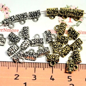 May include: A close-up of a variety of silver and gold metal end caps with decorative details. The end caps have a small loop at the top and are approximately 1 cm in length. The end caps are arranged on a ruler with markings in centimeters.