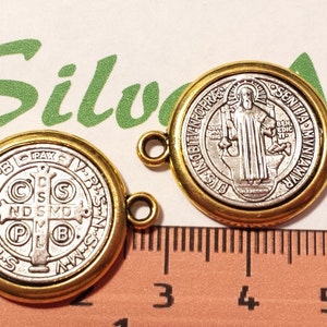 May include: Two gold-toned metal charms with a silver-toned Saint Benedict medal design. One charm features a cross with the letters 'C.S.S.M.L.  N.D.S.M.D.  P.B.' and the other charm features a standing figure of Saint Benedict.