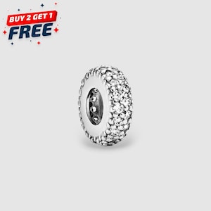 Könnte beinhalten: Ein silberfarbener Charm-Anhänger in Ringform, besetzt mit kleinen, klaren Kristallen. Der Charm hat ein detailliertes Design und ein zentrales Loch. Der Text "BUY 2 GET 1 FREE" ist oben links sichtbar.