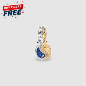 May include: A silver and gold charm with a yin-yang design. One side features a dark blue enamel with a crescent moon and stars, while the other side has a sunburst design with a central star. The charm is a jewelry item.