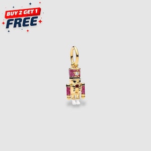 May include: A gold-colored charm in the shape of a toy soldier. The charm has a pink and gold hat, pink accents, and white feet. A small star-shaped gem is on the hat. The text "BUY 2 GET 1 FREE" is in the upper left corner.