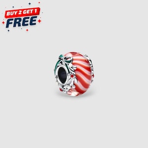 May include: A round charm with a red and white striped design, accented with a green bow and silver-coloured metal detailing. The charm has a central opening and is likely a bead for a bracelet or necklace.