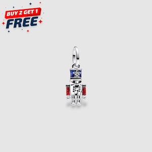 May include: A silver charm in the shape of a toy soldier. The soldier has a blue and red hat, red arms, and a silver body. The charm is hanging from a silver loop. Text in the upper left corner reads "BUY 2 GET 1 FREE".