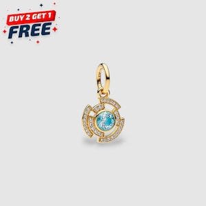 Puede incluir: Un colgante dorado con una piedra central azul claro, rodeada de cristales transparentes. El colgante tiene un diseño circular con una anilla para sujetarlo a una cadena. La imagen también incluye el texto "BUY 2 GET 1 FREE".