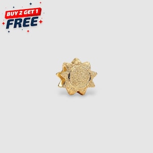 Puede incluir: Un dije dorado en forma de sol con una superficie texturizada. El dije tiene un centro circular y rayos puntiagudos. La imagen también incluye el texto "BUY 2 GET 1 FREE" en rojo, blanco y azul.