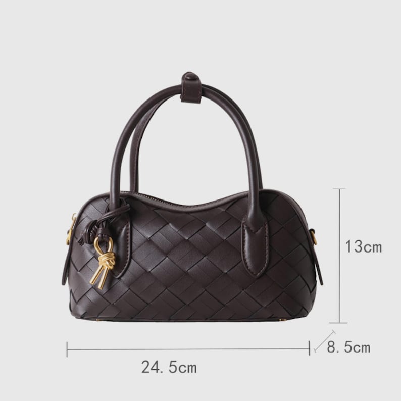 May include: A dark brown woven handbag with two handles and a gold-colored charm. The bag is 9.6 inches long, 5.1 inches high, and 3.3 inches wide.