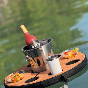 May include: A floating serving tray with a stainless steel ice bucket holding a bottle of red wine. The tray has a wooden surface with a black border, holding a white tumbler and two small bowls of fruit.