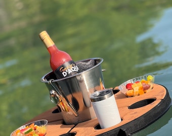 May include: A floating serving tray with a stainless steel ice bucket holding a bottle of red wine. The tray has a wooden surface with a black border, holding a white tumbler and two small bowls of fruit.