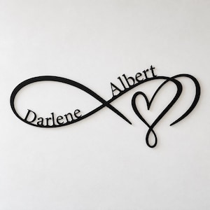 Può includere: Una decorazione da parete nera che presenta un simbolo dell'infinito intrecciato con una forma a cuore. Il nome Darlene è integrato nell'anello sinistro del simbolo dell'infinito, mentre il nome Albert è inserito sul lato destro del design.