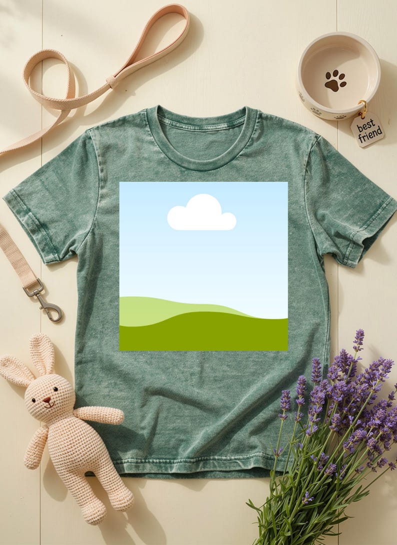May include: A green t-shirt with a landscape graphic featuring a blue sky, white cloud, and green hills. The image also includes a beige dog leash, a ceramic pet bowl with a paw print, a stuffed bunny, and lavender sprigs.