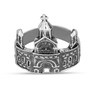 May include: A silver-colored ring featuring a detailed miniature church design. The ring showcases a central steeple with a cross, flanked by architectural elements. The ring's band is smooth, and the church design is intricately detailed.