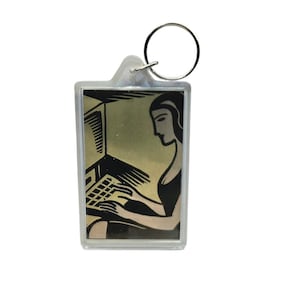 May include: A rectangular clear acrylic keychain featuring a black and beige graphic illustration of a person sitting at a computer. The design shows a side profile of the individual typing on a keyboard, with a metal ring attached at the top.