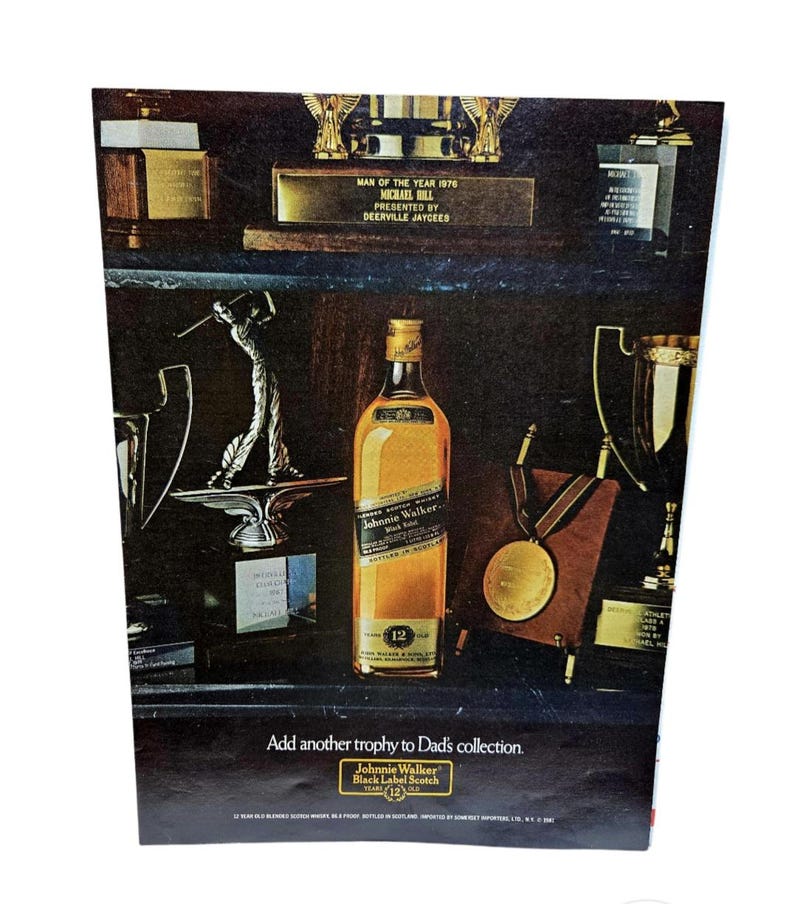 Puede incluir: Anuncio con una botella de whisky Johnnie Walker Black Label Scotch, rodeada de trofeos. El texto dice "A&ntilde;ade otro trofeo a la colecci&oacute;n de pap&aacute;" y "Hombre del A&ntilde;o 1976".