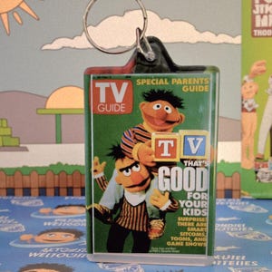 May include: A clear acrylic keychain featuring a TV Guide cover with the characters Bert and Ernie. The cover reads "That's Good For Your Kids" with the TV Guide logo. The keychain has a silver metal ring.