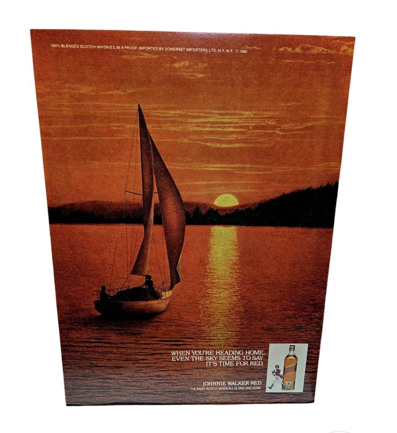 May include: An advertisement for Johnnie Walker Red featuring a sailboat on a lake at sunset. The sky and water are shades of orange and red. Text reads "When you're heading home, even the sky seems to say it's time for Red."