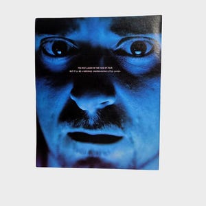 Könnte beinhalten: Nahaufnahme eines Gesichts, das in blauem Licht beleuchtet ist. Das Bild zeigt intensive Augen, einen Schnurrbart und den Text: "YOU MAY LAUGH IN THE FACE OF FEAR BUT IT'LL BE A NERVOUS, UNCONVINCING LITTLE LAUGH."