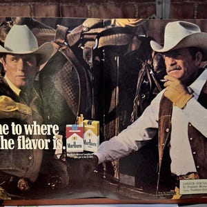May include: A vintage Marlboro advertisement featuring two individuals in cowboy hats, vests, and long-sleeved shirts. The text reads, "Come to where the flavor is." Two cigarette packs are displayed in the center, with a Surgeon General's warning.