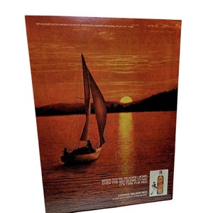 May include: An advertisement for Johnnie Walker Red featuring a sailboat on a lake at sunset. The sky and water are a warm orange. Text reads "When you're heading home even the sky seems to say it's time for red."