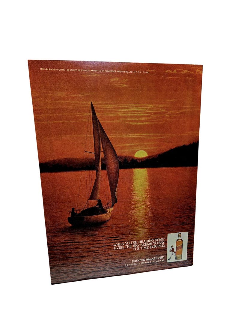May include: An advertisement for Johnnie Walker Red featuring a sailboat on a lake at sunset. The sky and water are a warm orange. Text reads "When you're heading home even the sky seems to say it's time for red."