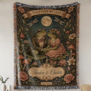 May include: A woven tapestry blanket featuring two frogs in formal attire holding hands on lily pads under a full moon. The design includes floral elements, mushrooms, dragonflies, and a banner with the text Together We Leap, Theodore & Charlotte, EST. 2022.