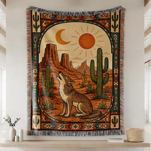 May include: A woven throw blanket featuring a desert landscape with a howling coyote, saguaro cacti, mesas, a sun, and a crescent moon. The design is framed by a decorative border with geometric patterns and fringe along the top and bottom edges.