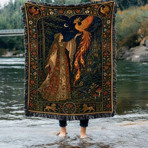 May include: A woven throw blanket featuring a detailed tapestry design of a person in a long, patterned robe reaching towards a golden phoenix. The scene includes a dark forest, a castle, and floral borders with lions, finished with fringed edges.