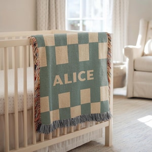 Könnte beinhalten: Eine personalisierte Babydecke mit einem Schachbrettmuster in Türkis und Beige, die über einem Kinderbett drapiert ist. Der Name "ALICE" ist in weißen Blockbuchstaben zu sehen. Die Decke hat einen mehrfarbigen Fransenrand.