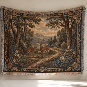 May include: A rectangular woven tapestry featuring a landscape scene with two deer standing on a dirt path. The border displays floral motifs in blue and gold. The central image shows trees, mountains, and a cloudy sky. The edges have fringe.