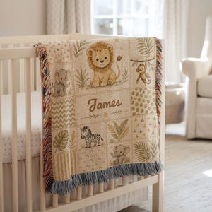 May include: A woven throw blanket featuring a grid pattern with illustrations of a lion, elephant, monkey, and zebra, along with tropical leaves and the name James in the centre. The blanket has a fringed edge and a beige, tan, and green colour palette.