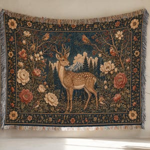 Könnte beinhalten: Eine rechteckige, gewebte Wandteppich-Decke mit einem zentralen Hirsch in einer Waldlandschaft mit Bergen, umgeben von großen cremefarbenen und roten Blüten, grünem Blattwerk und kleinen Vögeln, abgeschlossen mit einem gefransten Rand.