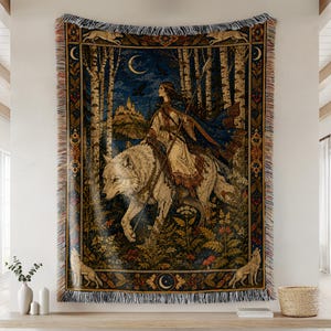 May include: A woven tapestry throw blanket featuring a person riding a large white wolf through a forest at night. The scene includes a crescent moon, a distant castle, and a decorative border with wolves and floral patterns, finished with fringe.