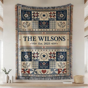 May include: A woven throw blanket featuring a patchwork design in navy blue, red, and cream. The centre panel displays the text THE WILSONS and Est. 2025. The pattern includes floral motifs, stars, gingham squares, and a heart, finished with fringed edges.