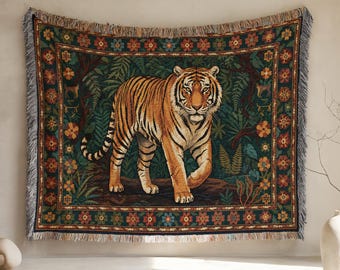 May include: A rectangular woven tapestry blanket featuring a central orange and black tiger standing in a lush green jungle setting. The design is framed by a dark green border decorated with repeating orange and red floral patterns and fringe.