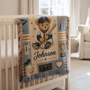 May include: A woven throw blanket featuring a baseball-themed design with a teddy bear in a uniform, a baseball bat, a trophy, and a scoreboard displaying the numbers 07, 5, and 03. The name Johnson is printed in blue script, with fringe edges.