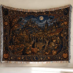 May include: A rectangular woven throw blanket featuring a detailed dark scene of a village at night with a full moon, pumpkins, black cats, and figures in pointed hats. The border includes pumpkin motifs and crescent moons with fringed edges.