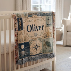 May include: A woven throw blanket featuring a nautical theme with the name Oliver centered in a decorative frame. The design includes a compass rose, a sea turtle, an anchor, seashells, and a moonlit ocean scene, finished with fringed edges.