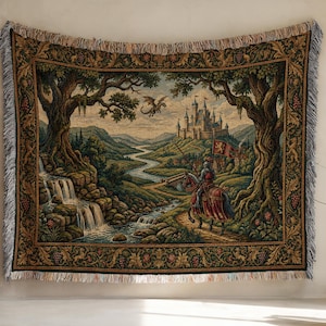 Könnte beinhalten: Eine gewebte Wandteppich-Decke mit einer mittelalterlichen Szene, die einen Ritter zu Pferd, eine Burg, einen fliegenden Drachen, einen Wasserfall und einen gewundenen Fluss zeigt. Der Rand ist mit einem Blatt- und Traubenmuster verziert.